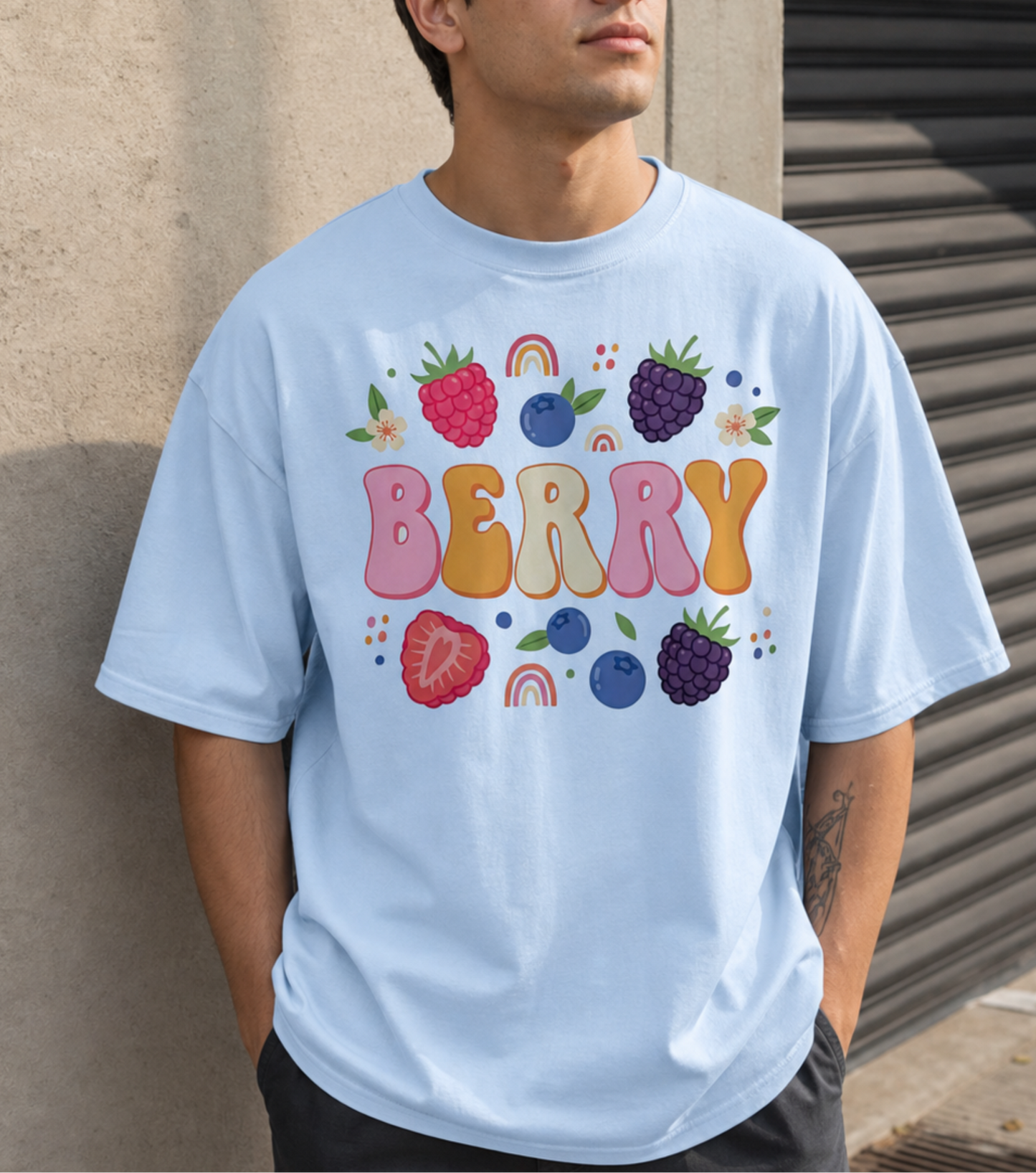 Man wearing a light blue t-shirt with colorful berry design against a textured wall.