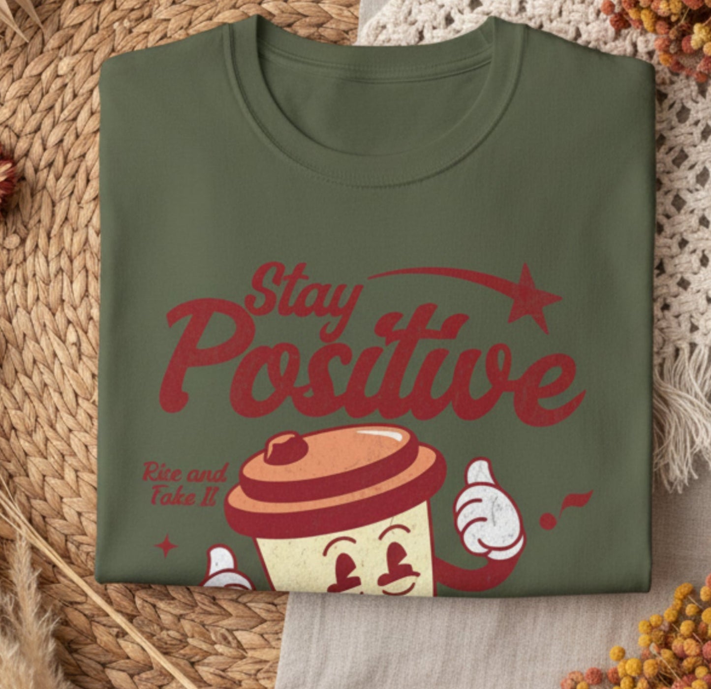 Folded green t-shirt with 'Stay Positive' and coffee graphic on a white background