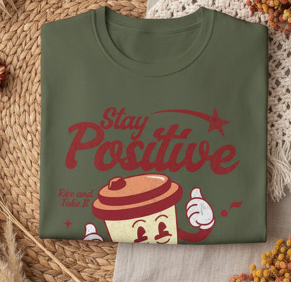 Folded green t-shirt with 'Stay Positive' and coffee graphic on a white background