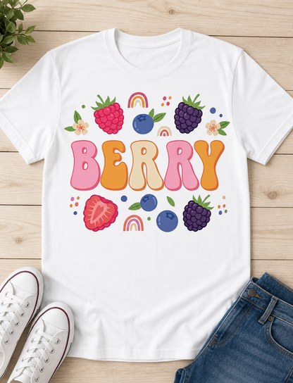 White t-shirt with colorful berry design and 'Berry' text on a wooden surface with shoes and jeans.