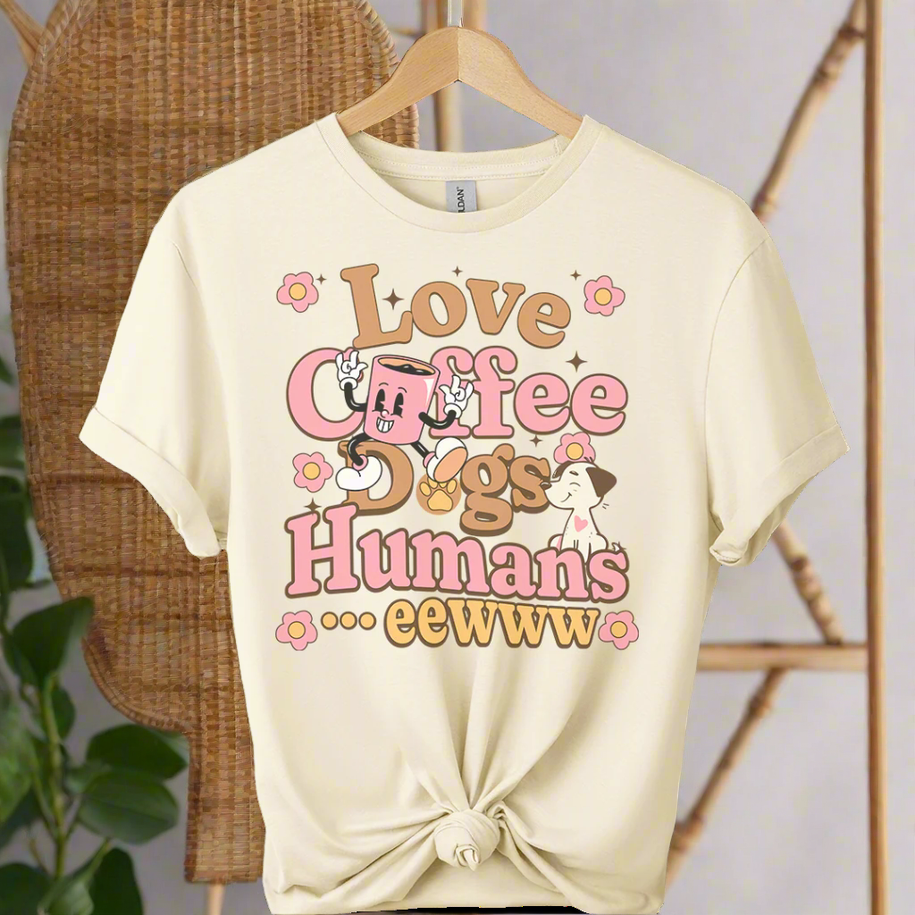 Beige t-shirt with 'Love Coffee, Dogs, Humans... eewww' text and cartoon characters on a hanger.