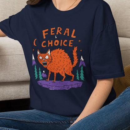 A woman sitting cross-legged on a woven rug in front of a beige couch, wearing a navy blue graphic t-shirt with an orange cat and the words 'FERAL CHOICE'.neilikha