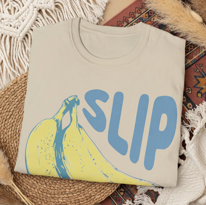 Folded sand t-shirt with a banana graphic and 'SLIP' text on a white background