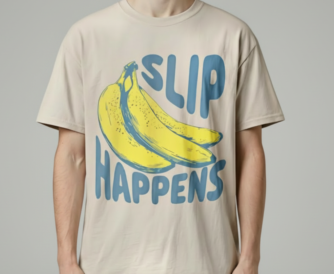 sand t-shirt with banana graphic and 'SLIP HAPPENS' text on a plain background