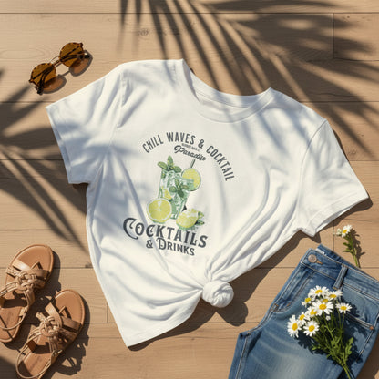 White t-shirt with cocktail graphic and text on a wooden surface with sunglasses, sandals, and flowers.