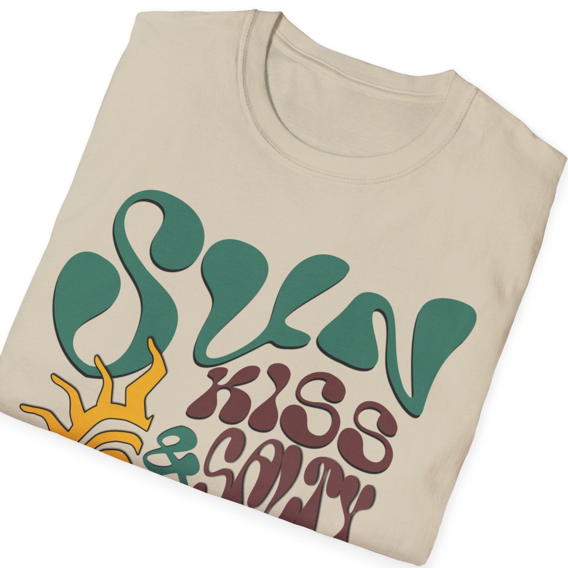 folded sand t-shirt featuring a wavy 70s groovy font graphic reading Sun Kissed and Salty Like My Attitude with a sun drawing