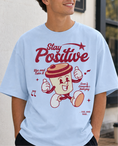 men wearing a light blue t-shirt with a cartoon character and 'Stay Positive' text.