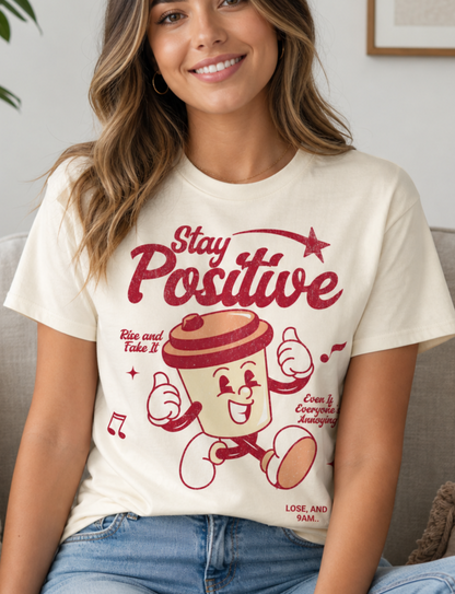 Woman wearing a 'Stay Positive' t-shirt with a cartoon character in a living room.